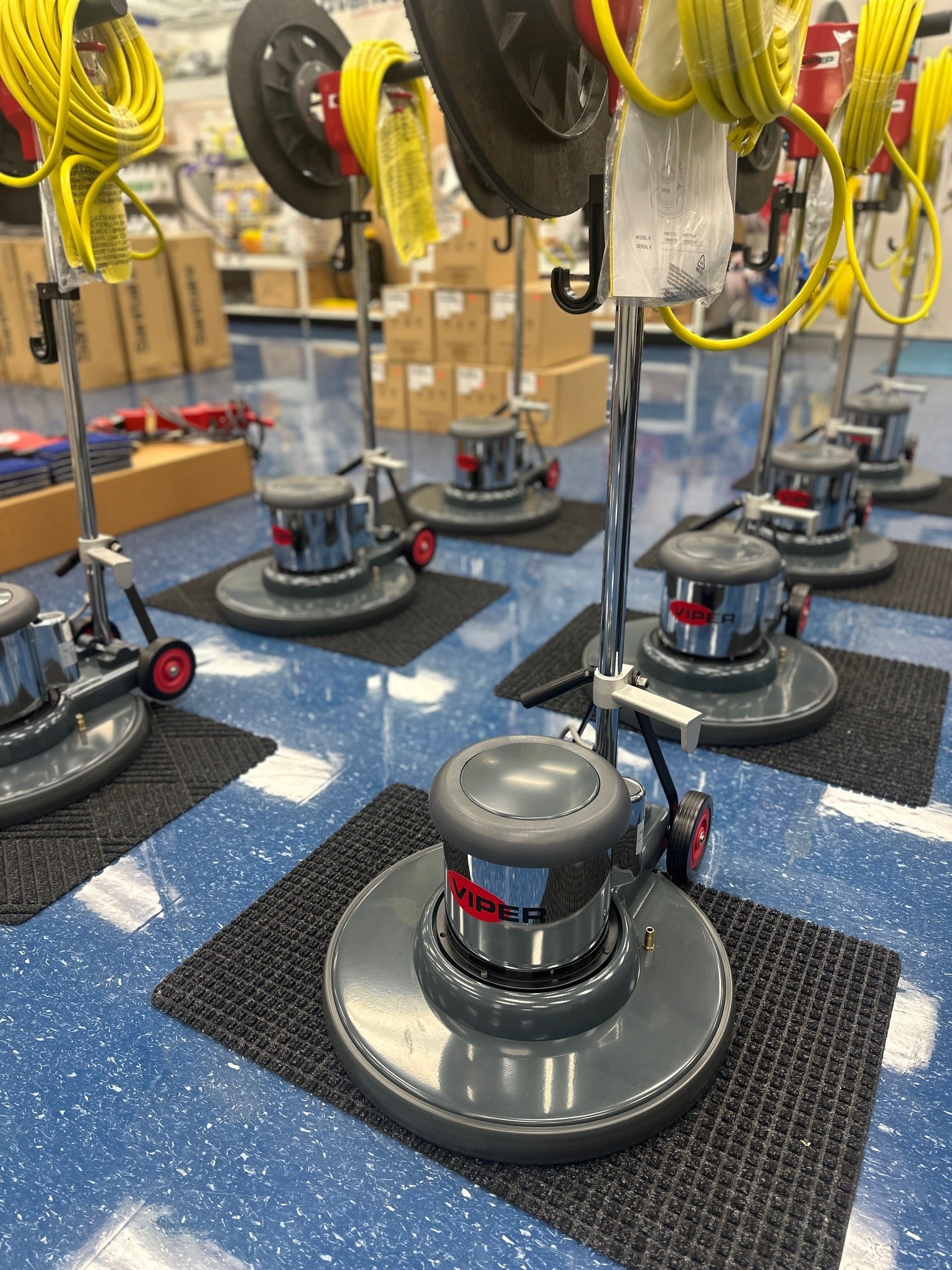 Floor polishing machines on a blue floor with boxes in the background